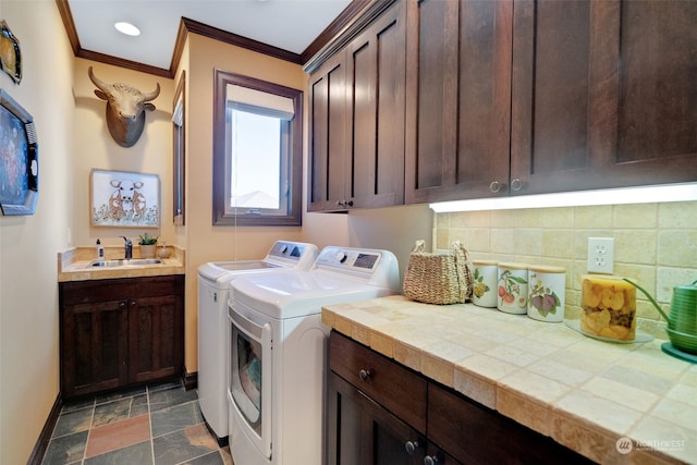 clothes washing area with ornamental molding, cabinets, sink, and washing machine and clothes dryer