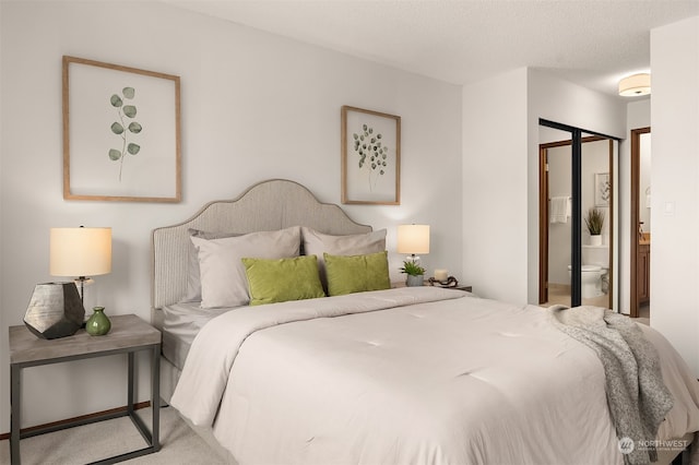 carpeted bedroom featuring a textured ceiling and ensuite bath