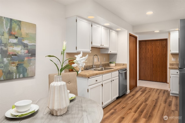 kitchen with stainless steel dishwasher, sink, white cabinetry, and light hardwood / wood-style floors