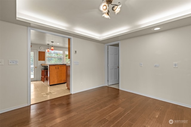 unfurnished living room with light wood-type flooring, a tray ceiling, and an inviting chandelier