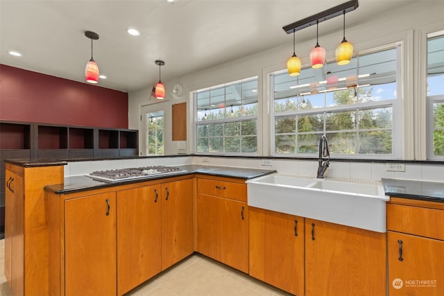 kitchen featuring kitchen peninsula, light tile patterned floors, decorative light fixtures, stainless steel gas stovetop, and sink