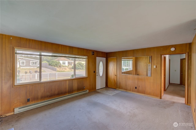 carpeted empty room with a wealth of natural light, baseboard heating, and wooden walls