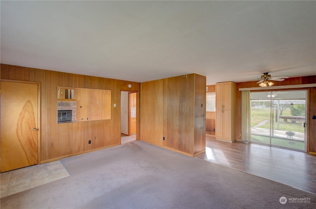 spare room with light colored carpet, ceiling fan, wood walls, and a fireplace