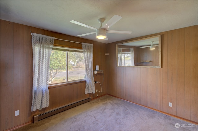 unfurnished room with light carpet, baseboard heating, wood walls, and ceiling fan