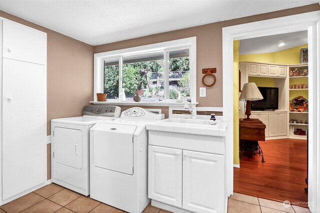 laundry area with sink, light tile patterned floors, a textured ceiling, washer and clothes dryer, and cabinets