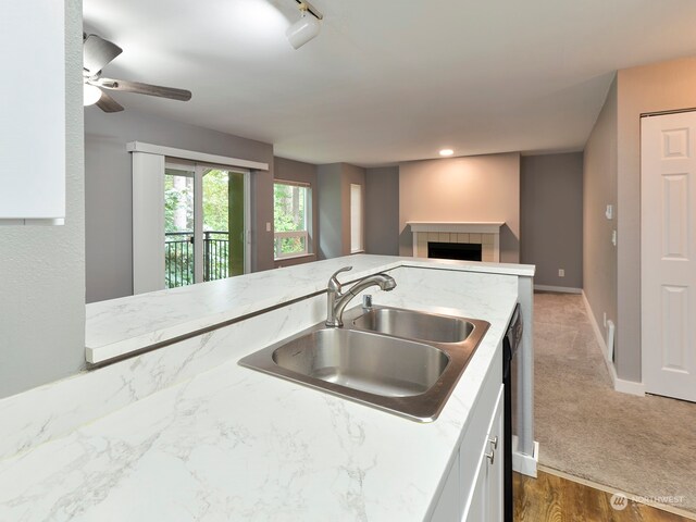 kitchen featuring white cabinets, carpet floors, a tile fireplace, ceiling fan, and sink