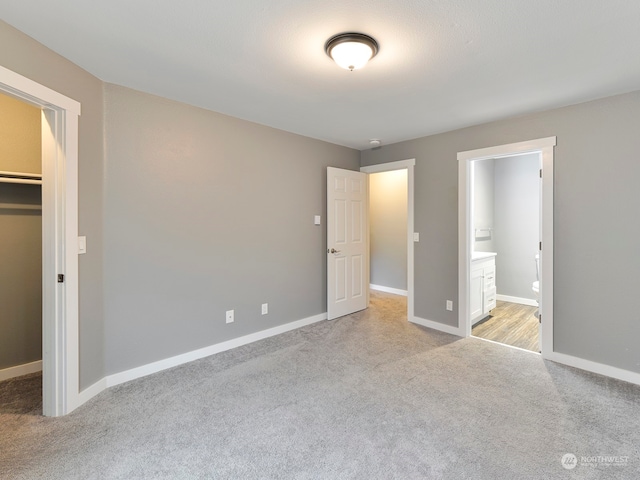 unfurnished bedroom with light colored carpet, connected bathroom, a walk in closet, and a closet