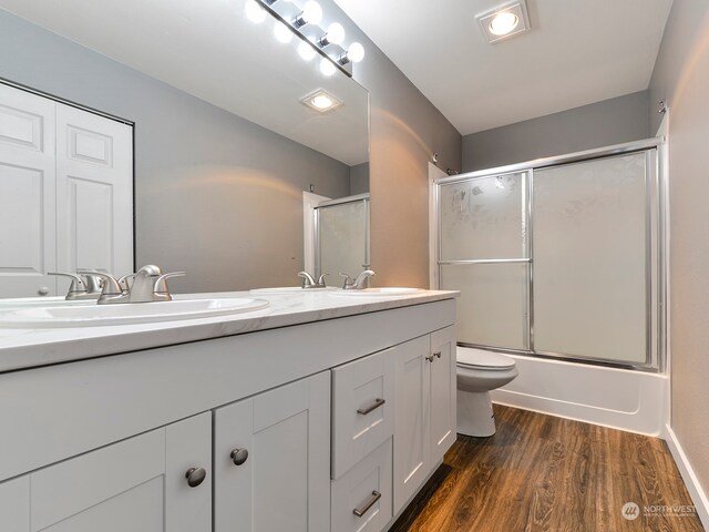 full bathroom with wood-type flooring, enclosed tub / shower combo, vanity, and toilet