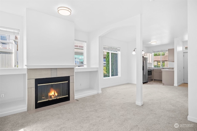 unfurnished living room with light carpet, a tile fireplace, and sink