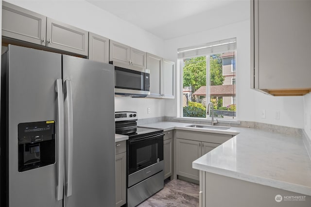 kitchen featuring light stone counters, appliances with stainless steel finishes, sink, and gray cabinetry