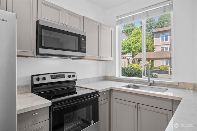 kitchen featuring appliances with stainless steel finishes, gray cabinetry, sink, and light stone countertops