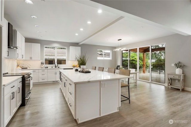 kitchen featuring a center island, white cabinets, wall chimney range hood, decorative light fixtures, and stainless steel electric range