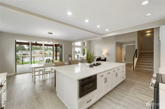 kitchen with hanging light fixtures, white cabinetry, a center island, light stone countertops, and light hardwood / wood-style floors