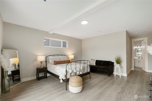 bedroom with connected bathroom, beamed ceiling, and light wood-type flooring