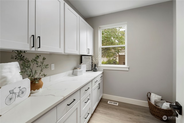 interior space with light wood-type flooring, light stone counters, and white cabinets