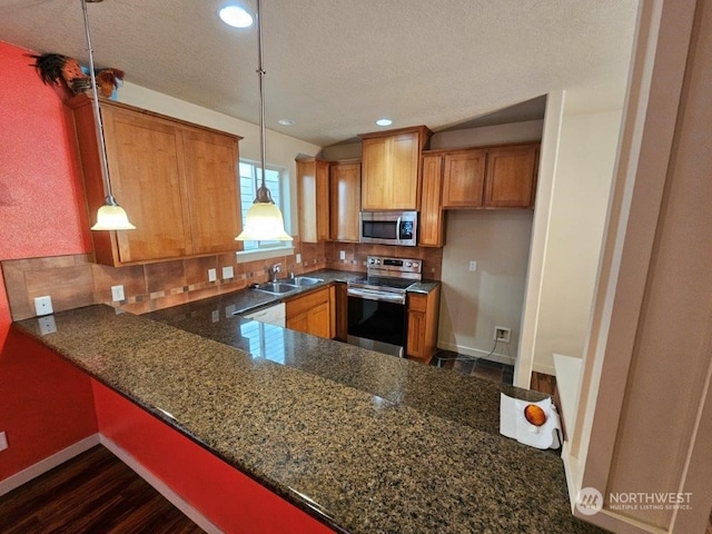 kitchen featuring dark hardwood / wood-style floors, decorative light fixtures, appliances with stainless steel finishes, kitchen peninsula, and dark stone countertops