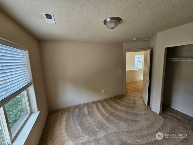 unfurnished bedroom featuring a textured ceiling, light colored carpet, and a closet