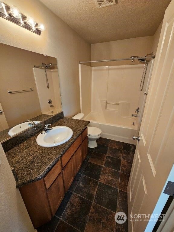 full bathroom featuring toilet, tub / shower combination, a textured ceiling, and vanity