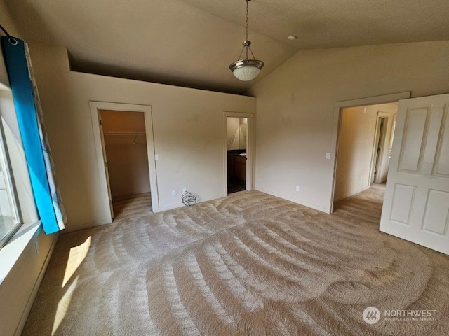 unfurnished bedroom featuring a walk in closet, light colored carpet, a closet, and vaulted ceiling