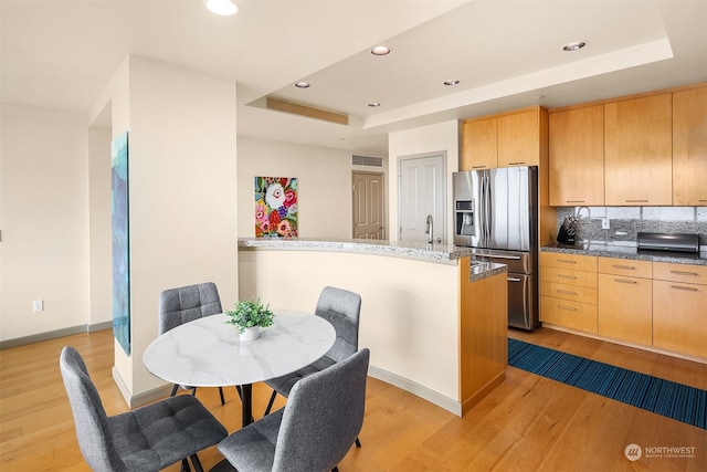 kitchen featuring a tray ceiling, light hardwood / wood-style floors, stainless steel fridge with ice dispenser, tasteful backsplash, and light brown cabinetry