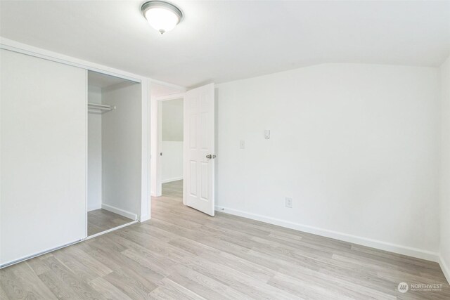 unfurnished bedroom featuring light wood-type flooring, vaulted ceiling, and a closet