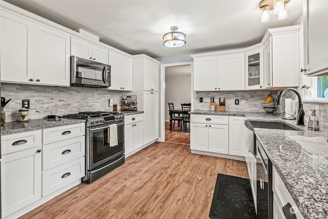 kitchen with white cabinets, light hardwood / wood-style flooring, light stone countertops, stainless steel appliances, and tasteful backsplash