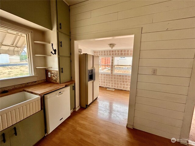 kitchen with butcher block countertops, stainless steel refrigerator with ice dispenser, white dishwasher, light hardwood / wood-style flooring, and wooden walls