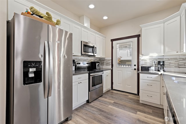 kitchen with decorative backsplash, stainless steel appliances, white cabinets, and light wood-type flooring