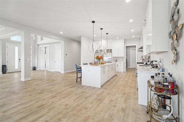 kitchen featuring light hardwood / wood-style floors, white cabinets, stainless steel refrigerator, a center island, and decorative light fixtures