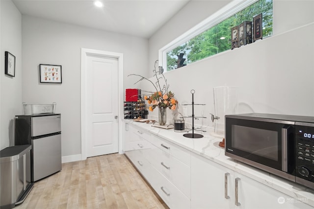 kitchen featuring light stone countertops, appliances with stainless steel finishes, light wood-type flooring, and white cabinetry