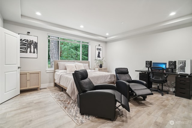 bedroom with light hardwood / wood-style floors and a raised ceiling