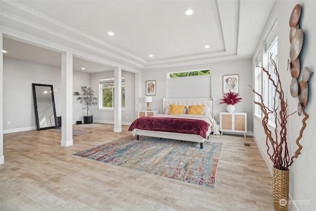 bedroom with light hardwood / wood-style flooring, decorative columns, and a raised ceiling