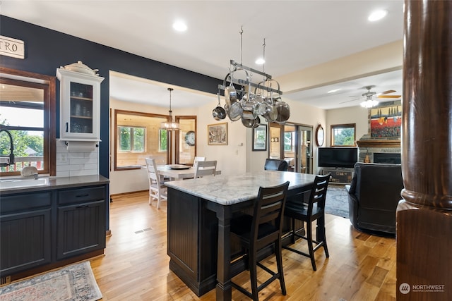 kitchen featuring ceiling fan with notable chandelier, a stone fireplace, a kitchen bar, decorative backsplash, and light wood-type flooring