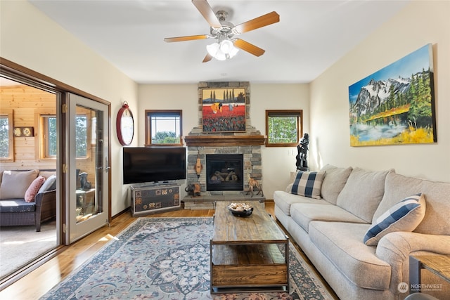 living room featuring light hardwood / wood-style flooring, ceiling fan, a stone fireplace, and wooden walls