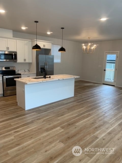 kitchen with appliances with stainless steel finishes, white cabinetry, a center island with sink, and light hardwood / wood-style floors