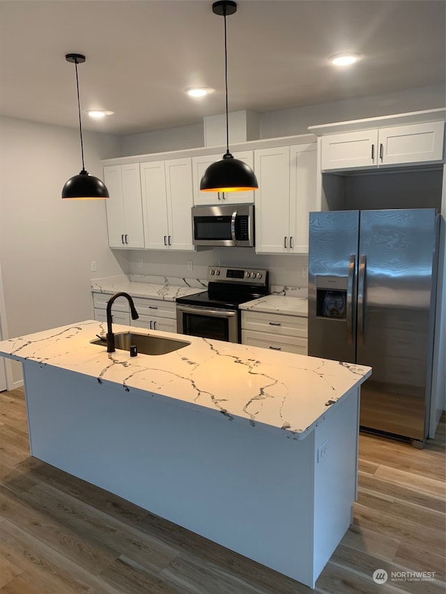 kitchen with appliances with stainless steel finishes, hanging light fixtures, an island with sink, and light hardwood / wood-style flooring