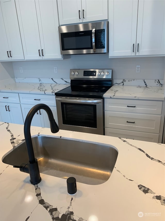 kitchen with stainless steel appliances, sink, light stone countertops, and white cabinetry