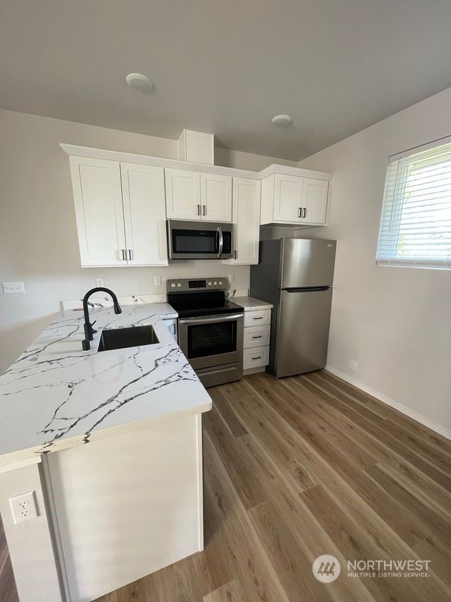 kitchen with light stone countertops, stainless steel appliances, white cabinetry, sink, and wood-type flooring