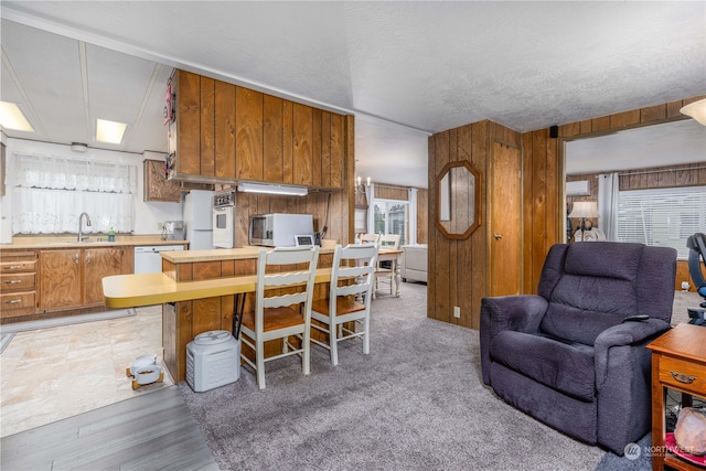 kitchen featuring a textured ceiling, wood walls, white appliances, sink, and light wood-type flooring