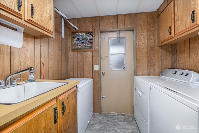 washroom featuring wood walls, cabinets, washer and clothes dryer, and sink