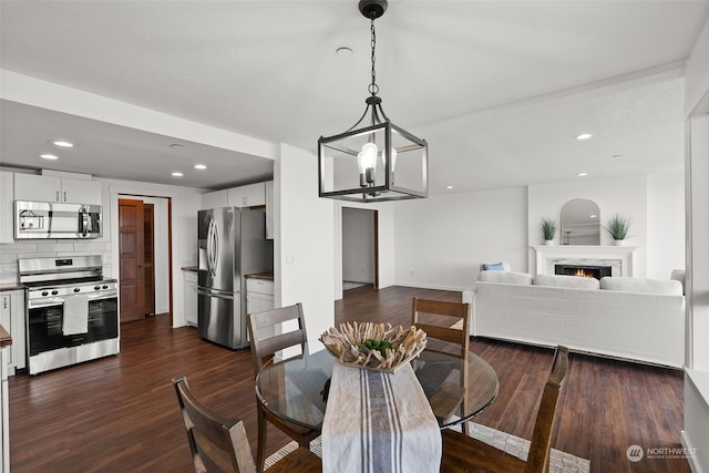 dining room featuring dark wood-style floors, a lit fireplace, a chandelier, recessed lighting, and baseboards