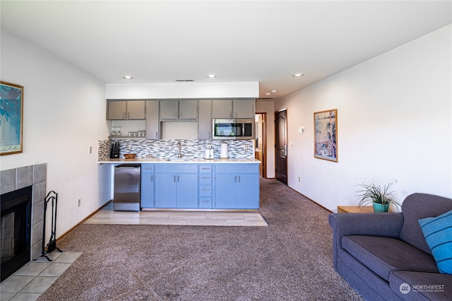 kitchen featuring a tile fireplace, sink, light carpet, decorative backsplash, and gray cabinetry