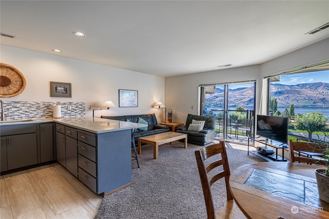 kitchen featuring gray cabinetry, tasteful backsplash, kitchen peninsula, light wood-type flooring, and sink