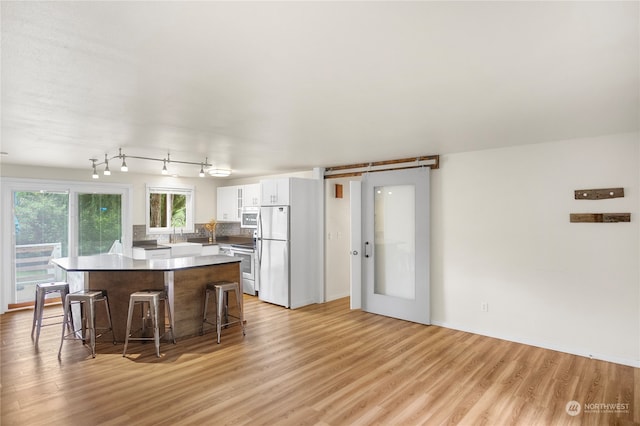 kitchen with white cabinetry, stainless steel appliances, a center island, light wood-type flooring, and a kitchen bar