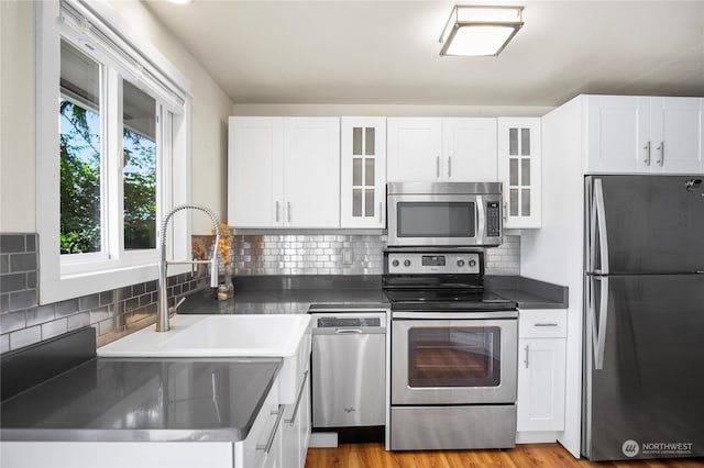 kitchen with appliances with stainless steel finishes, white cabinets, backsplash, light hardwood / wood-style flooring, and sink