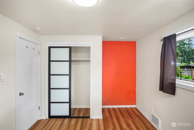 unfurnished bedroom featuring multiple windows, hardwood / wood-style floors, and a closet