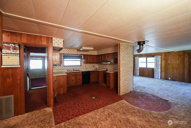 kitchen featuring backsplash, wood walls, dishwasher, sink, and dark colored carpet