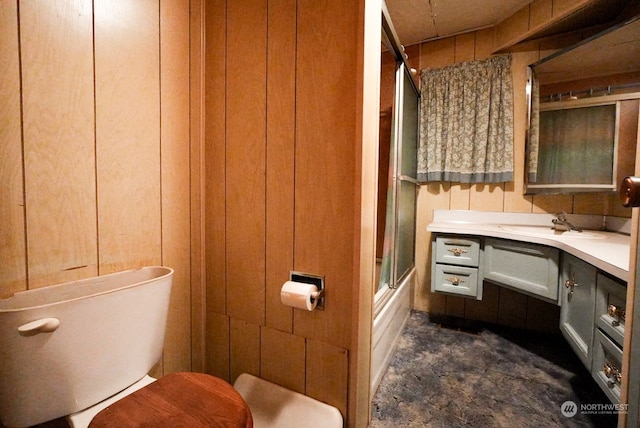 full bathroom with enclosed tub / shower combo, toilet, wooden walls, and vanity