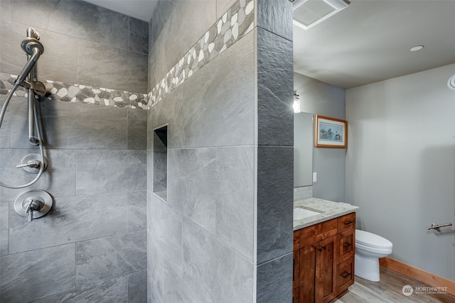 bathroom with toilet, hardwood / wood-style floors, vanity, and a tile shower