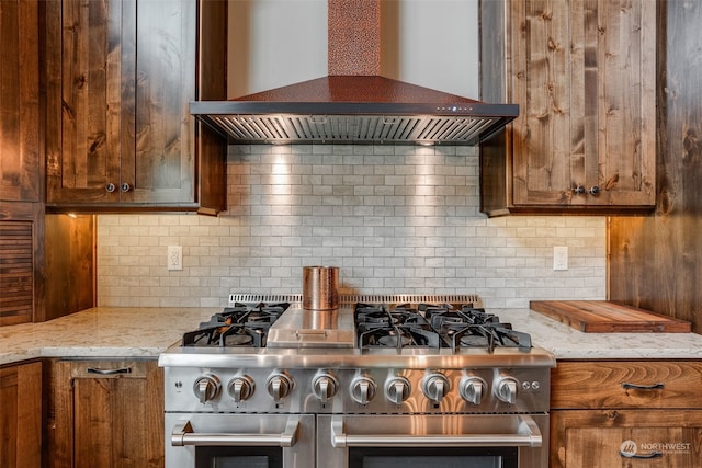 kitchen featuring wall chimney range hood, light stone counters, decorative backsplash, and high end stove